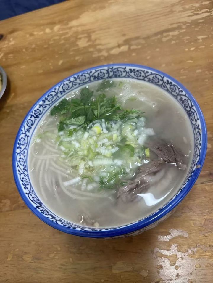 A bowl of clear lamb offal soup with glass noodles, lamb, scallions and cilantro